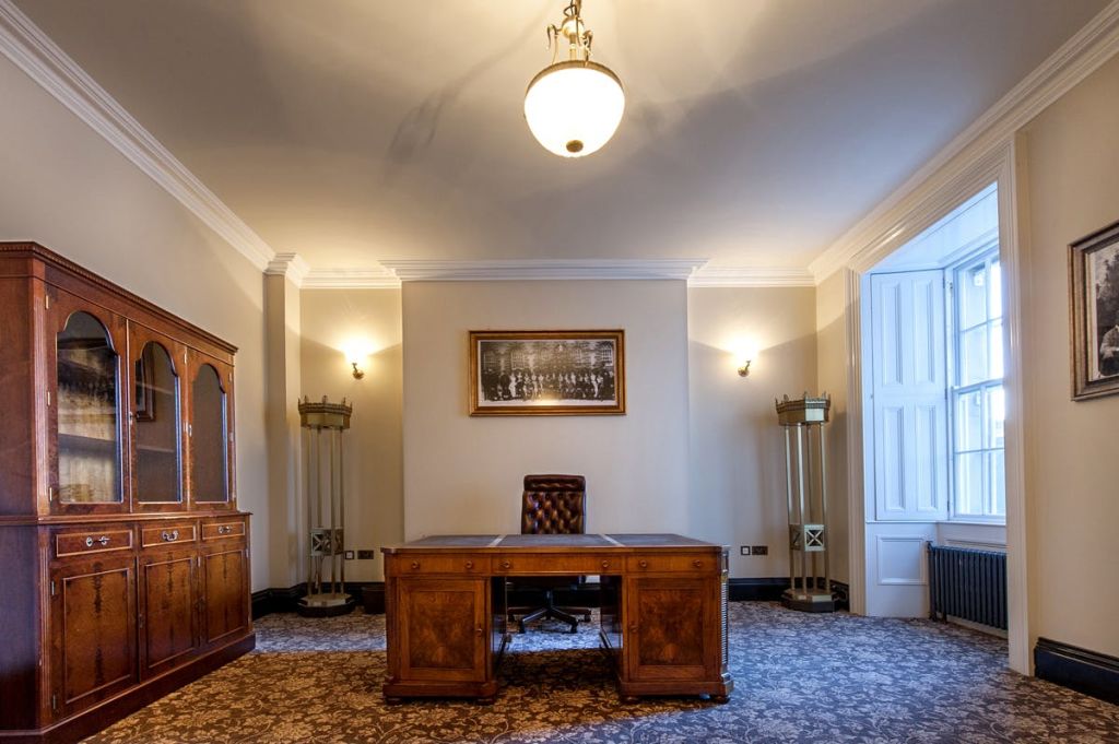 나무 책상과 가죽 의자, 화려한 카펫, 액자에 담긴 빈티지 사진, 샹들리에 조명이 있는 클래식한 사무실입니다.