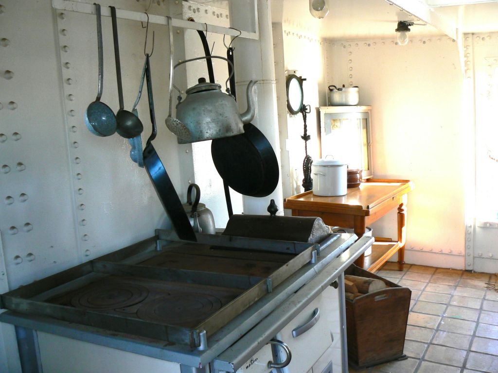 식기, 주전자, 가스레인지, 나무 테이블, 표면과 선반에 놓인 다양한 주방용품이 있는 빈티지 주방입니다.