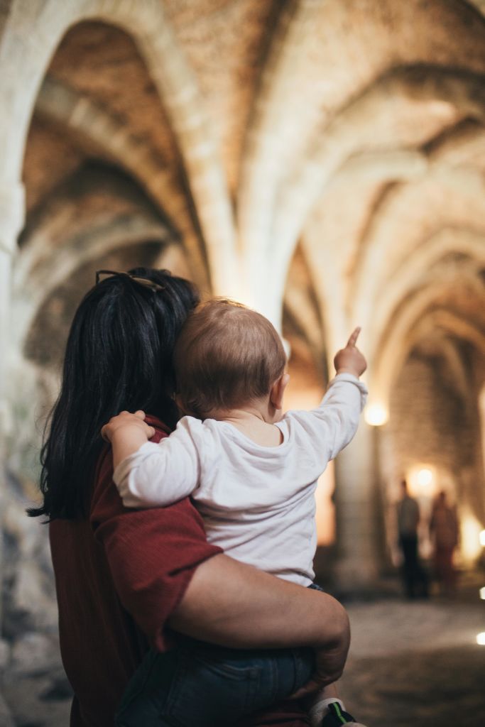 조명이 어두운 아치형 성당 내부에서 아기를 안고 있는 사람으로, 아기가 프레임 밖의 무언가를 가리키고 있습니다.