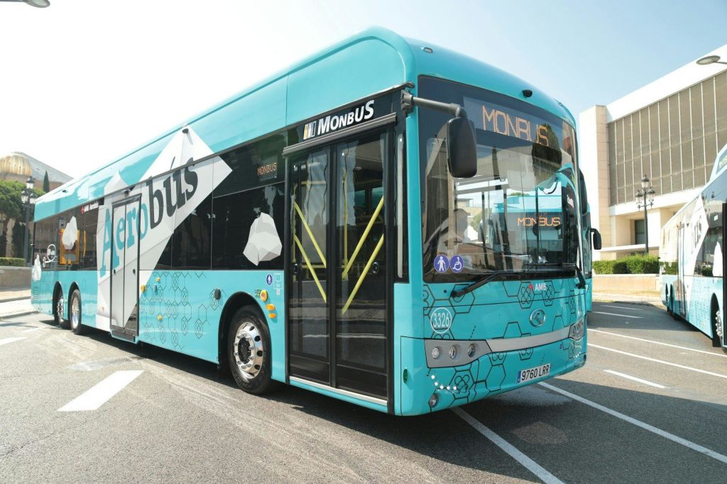 "Monbus" 라고 표시된 밝은 청록색 버스가 문이 열린 버스 정류장에 주차되어 있습니다.