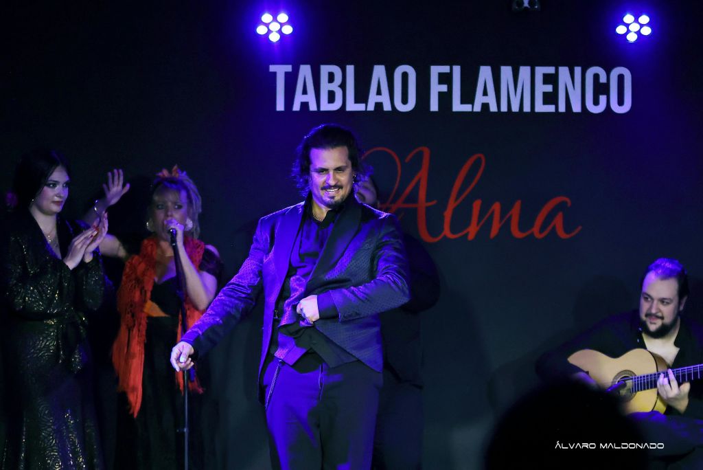 플라멩코 쇼 무대에서 두 명의 공연자가 공연합니다. 하나는 'Tablao Flamenco Alma' 를 배경으로 노래를 부르고 다른 하나는 기타를 연주하고 있습니다.