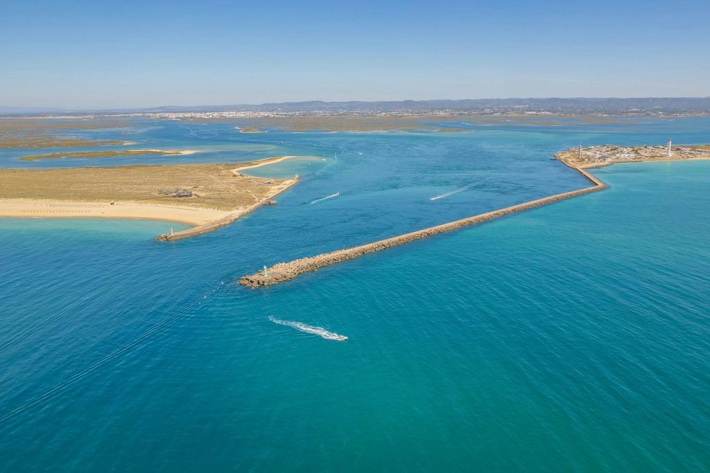 맑고 푸른 하늘 아래 청록색 바다에 보트가 있는 모래 해변, 부두, 등대의 해안 공중 전망.