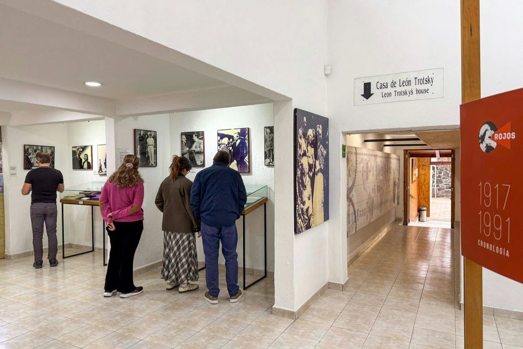 세 사람이 '카사 데 레온 트로츠키' 라는 라벨이 붙은 박물관의 전시물을 살펴보고 있습니다.'벽에는 사진과 역사 정보가 표시됩니다.