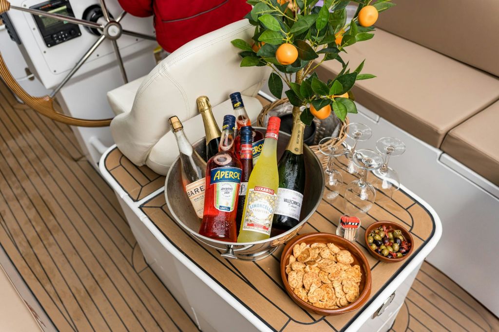 와인잔이 놓인 요트 데크 테이블에는 양동이에 담긴 다양한 음료와 간식, 작은 감귤류가 놓여 있습니다.
