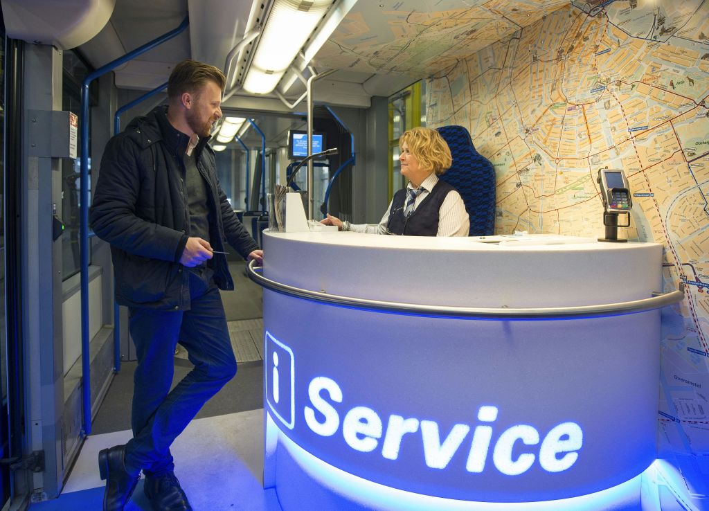 벽에 지도가 있는 현대적인 공간 내부의 조명 서비스 데스크에서 한 남성이 여성과 이야기를 나누고 있습니다.