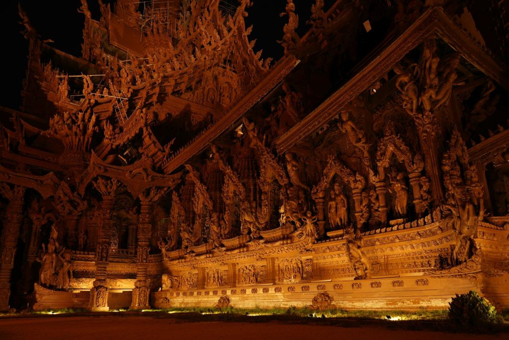 복잡한 패턴과 조각이 있는 정교하게 조각된 목조 사원 외관, 야간 조명.
