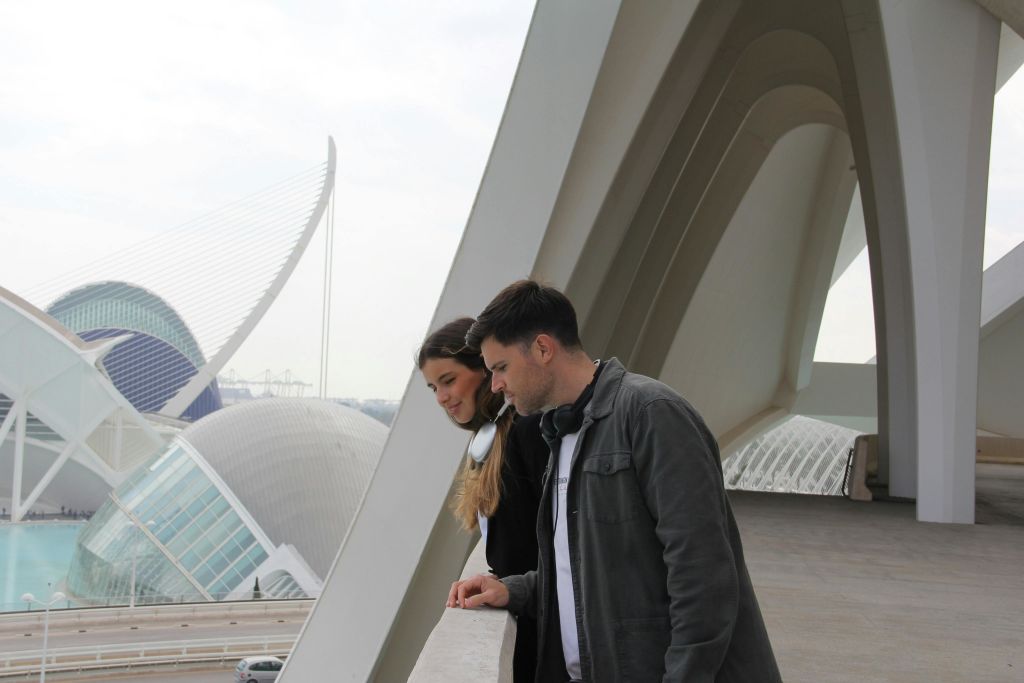 두 사람은 현대적인 구조에 기대어 있으며, 곡선형의 현대적인 건물을 배경으로 하고 있습니다.