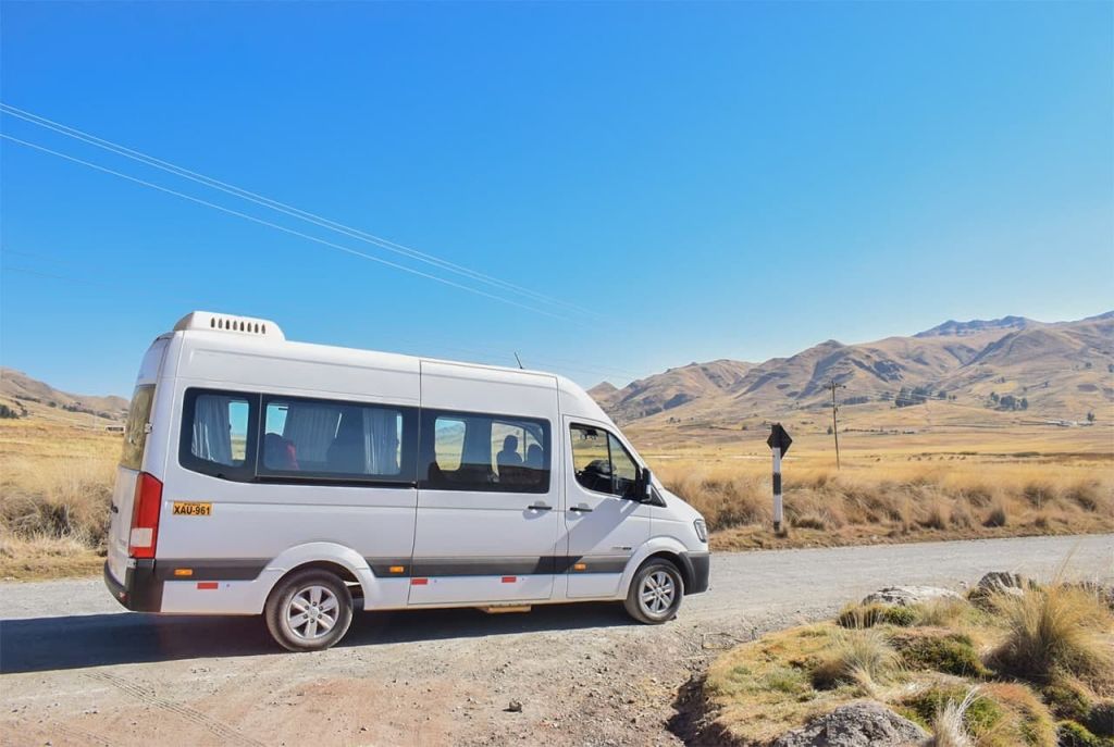 산과 맑고 푸른 하늘을 배경으로 시골의 흙길에 하얀 미니버스.