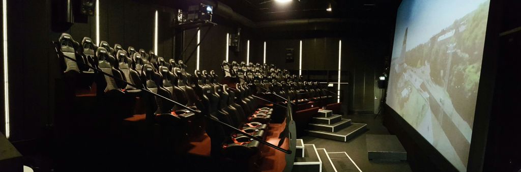 검은색과 빨간색 모션 시트가 여러 줄로 늘어선 조명이 희미한 극장으로, 프로젝터와 스크린 공간을 마주보고 있습니다.