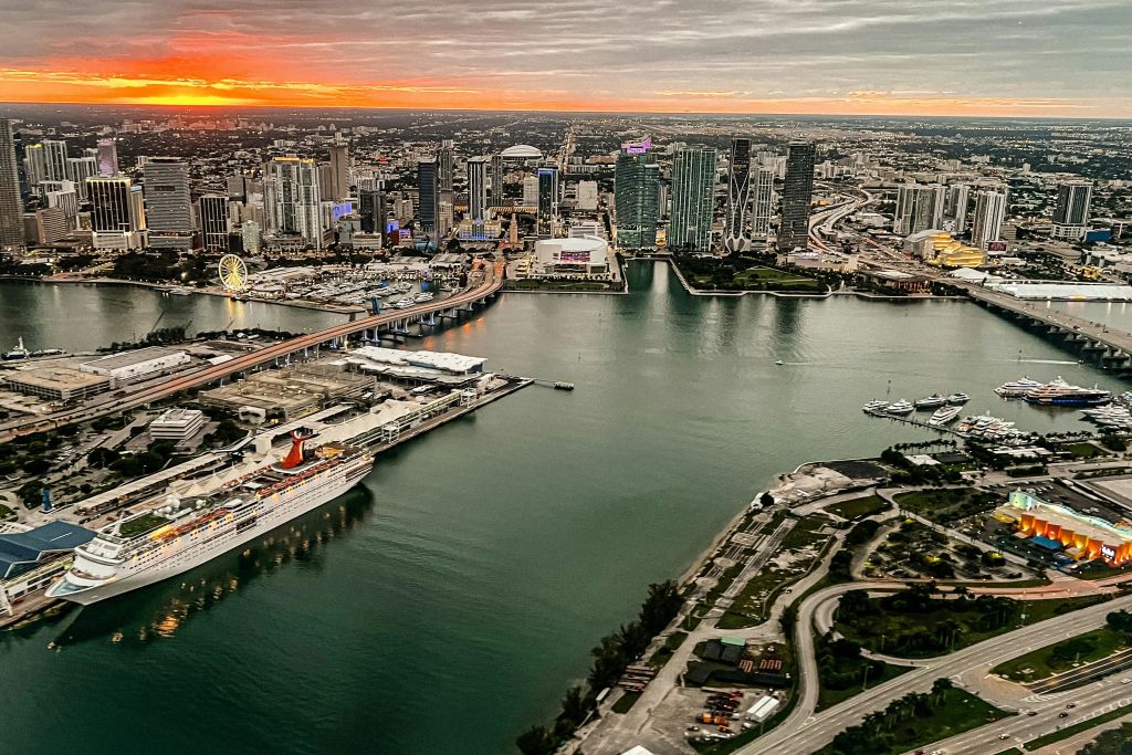 해가 질 무렵 고층 건물, 다리, 정박한 유람선, 수변 지역이 있는 도시 풍경의 공중 전경.