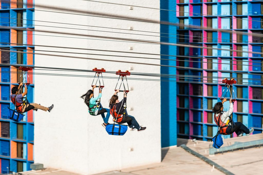 파란색, 분홍색, 검은색으로 강조된 화려한 건물 외관 근처에 집라인이 있습니다.