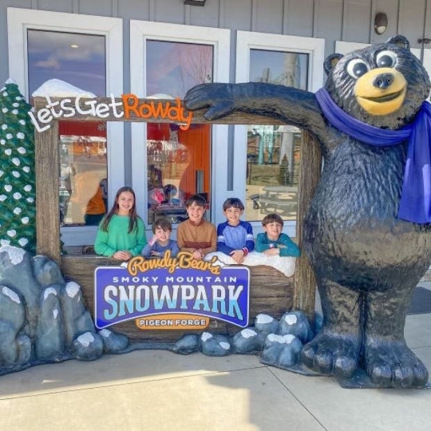 커다란 곰 조각상 옆에 있는 '라우디 베어 스모키 마운틴 스노우파크 (Rowdy Bear's Smoky Mountain Snowpark)' 의 나무 표지판 뒤에서 다섯 명의 어린이가 포즈를 취