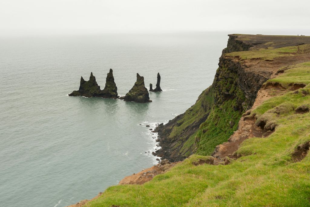 바다가 내려다보이는 절벽과 흐린 하늘 아래 물에서 나오는 세 개의 들쭉날쭉한 바위 지층.