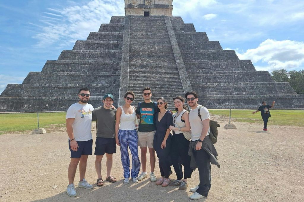 푸른 하늘 아래 커다란 석조 피라미드 앞에서 포즈를 취하고 있는 한 무리의 사람들.