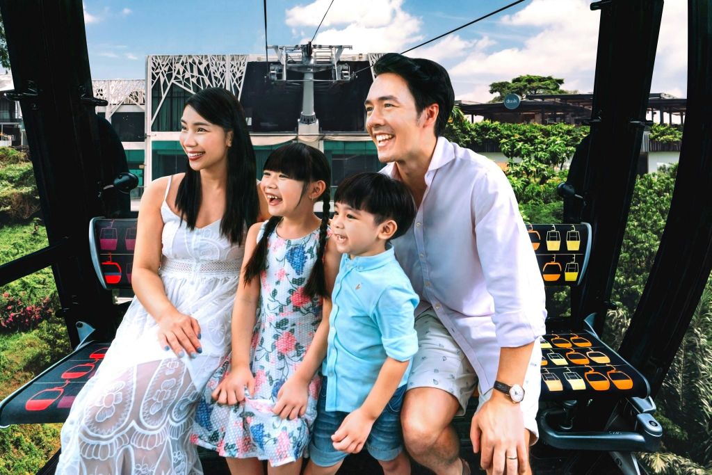 건물과 푸른 하늘을 배경으로 케이블카를 네 대나 타는 웃는 가족.