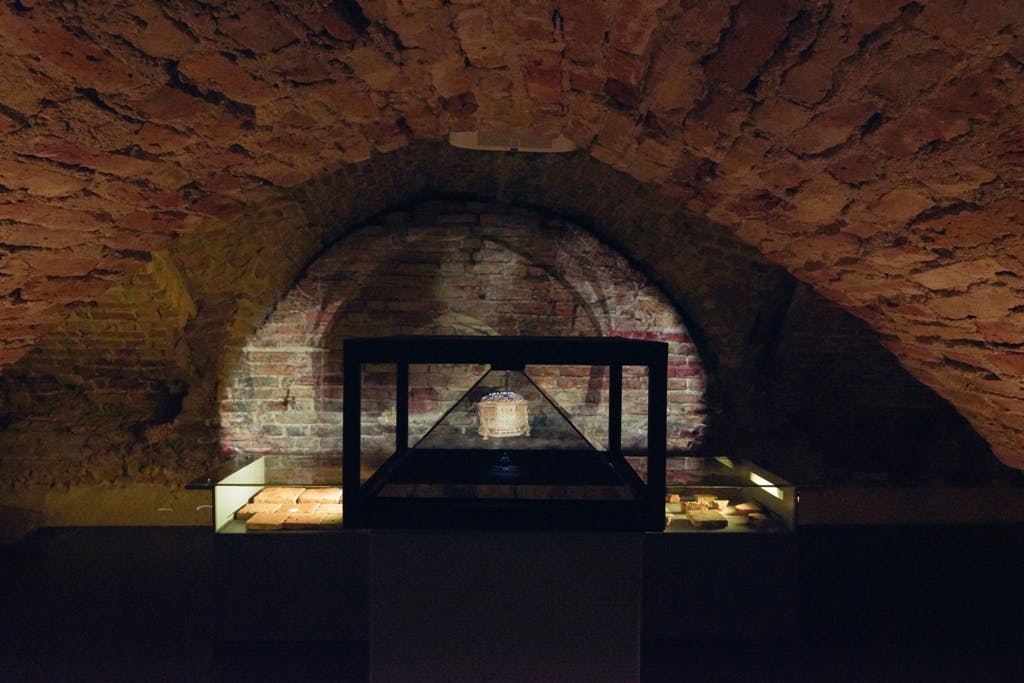 조명이 켜진 벽돌 벽으로 둘러싸인 공간으로, 조명이 켜진 선반 옆에는 유물을 담은 조명 디스플레이 케이스가 놓여 있습니다.