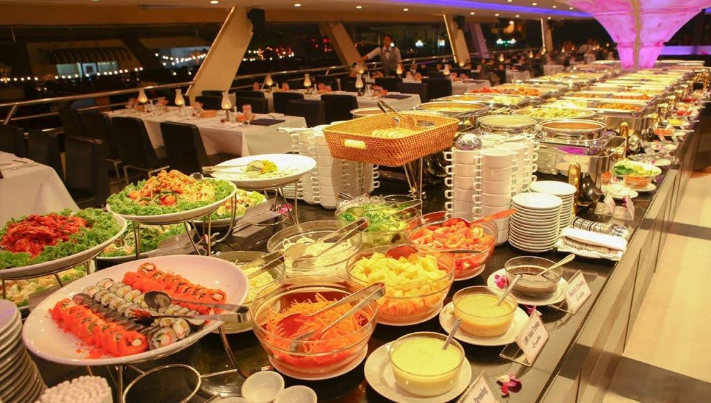 다양한 샐러드, 과일, 소스를 그릇에 담아 뷔페식으로 즐길 수 있습니다. 식탁과 의자가 배경으로 마련되어 있습니다.