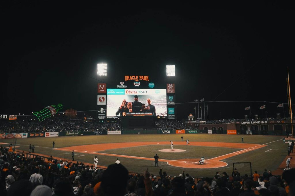 오라클 파크에서 야간 야구 경기가 열리고 점수판이 켜지고 스탠드에서 관중들이 경기를 관람합니다.