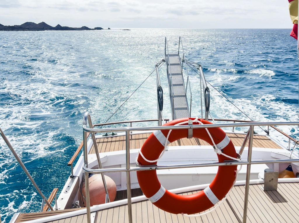 붉은 구명 부표, 바다로 이어지는 금속 사다리, 수평선에 있는 먼 암석이 있는 보트 갑판.