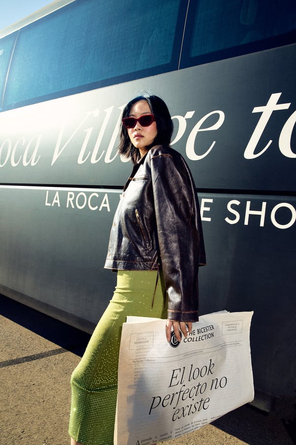 가죽 재킷과 선글라스를 착용한 사람이 "라 로카 빌리지" 가 적힌 버스 앞에 서 있습니다.