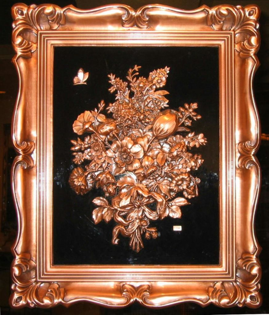 구리색 꽃무늬가 돋보이는 화려한 나무 프레임과 검은색 배경에 작은 나비가 있습니다.