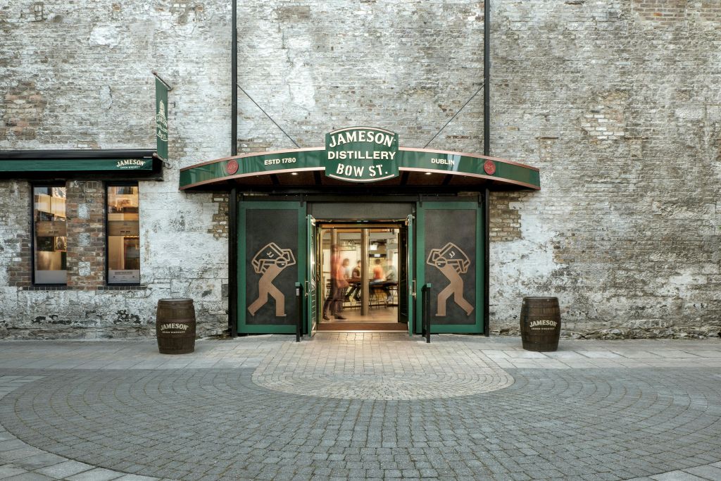 녹색 문, 위스키 통 장식, 내부의 사람들이 보이는 Jameson Distillery Bow St. 입구.