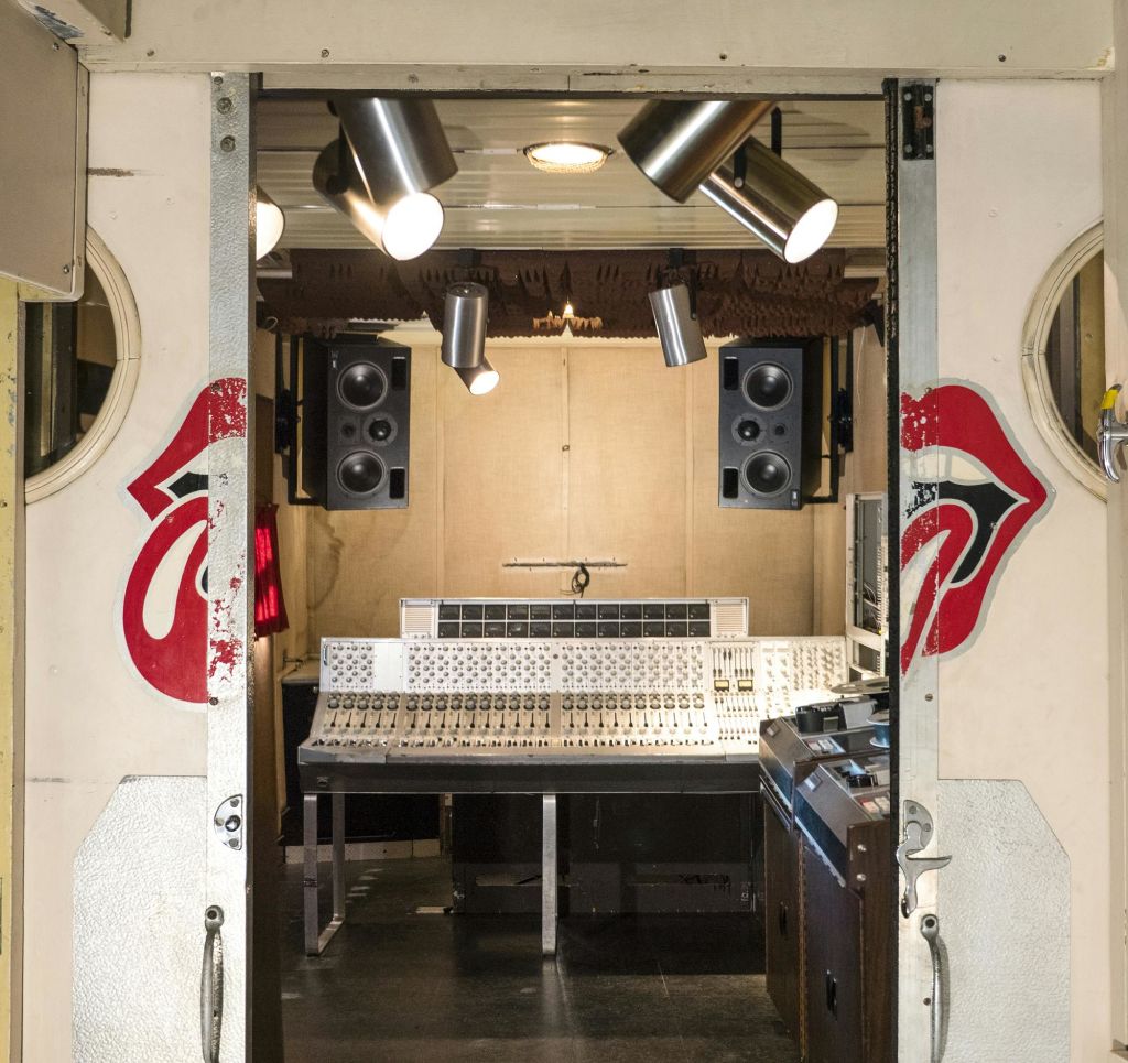 믹싱 콘솔, 스피커, 오버헤드 조명을 갖춘 녹음 스튜디오로, 문에 빨간 입술 로고가 그려져 있습니다.