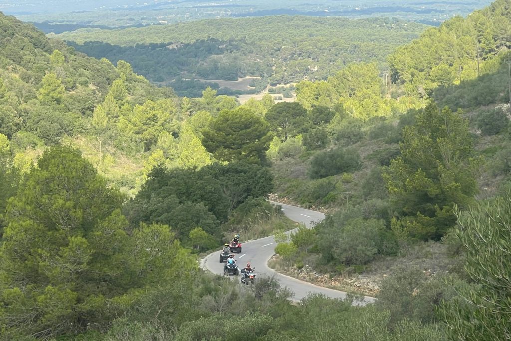 오토바이 운전자들은 언덕을 배경으로 빽빽하고 푸른 숲으로 둘러싸인 구불구불한 도로를 달립니다.