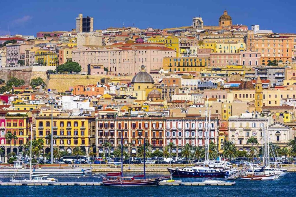 맑고 푸른 하늘 아래, 알록달록한 건물과 돔, 배가 정박해 있는 해안 도시 풍경.