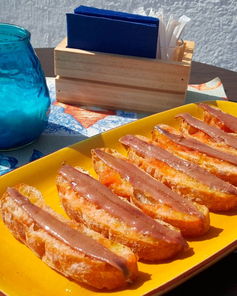 파란색 유리병과 나무 냅킨 홀더 옆에 노란색 접시에 붉은 갈색을 얹은 구운 빵 조각.