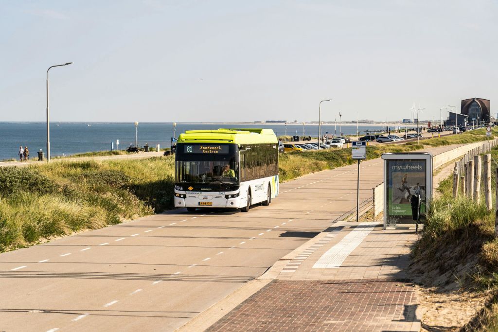 녹색과 흰색 버스가 해안 도로를 따라 한쪽에는 잔디가 우거진 모래 언덕이 있고, 바다를 배경으로 운행됩니다.