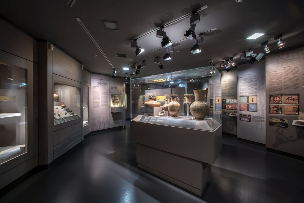 유리 케이스에 고대 도자기를 전시한 박물관 전시관으로, 위에 정보 패널과 스포트라이트가 있습니다.