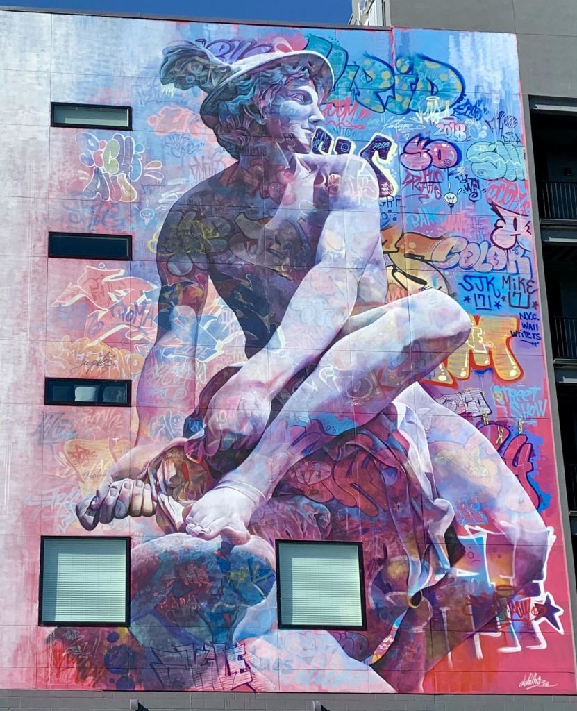 활기찬 그래피티 아트와 패턴이 겹쳐진 커다란 조각상 같은 인물이 있는 건물의 다채로운 벽화입니다.