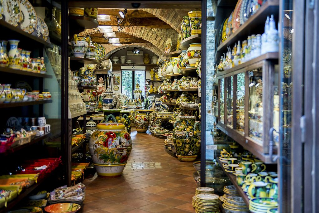 선반과 테이블에 화려한 도자기로 가득 찬 도자기 가게로, 꽃병, 접시 및 다양한 도자기 조각이 있습니다.