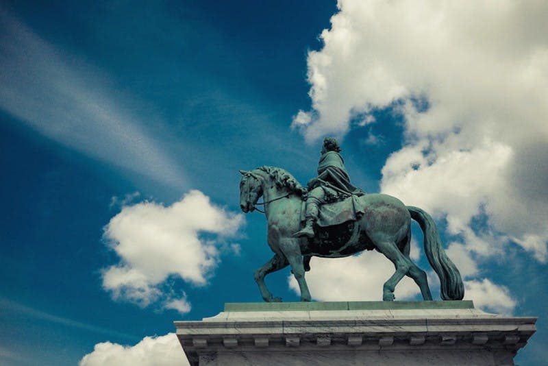 구름이 흩어져 있는 푸른 하늘을 배경으로 받침대에 달린 겉옷을 입은 모습의 청동 승마 동상.