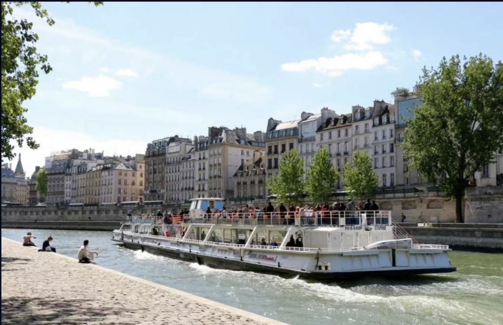 승객이 탑승한 투어 보트는 부분적으로 흐린 하늘 아래 역사적인 건물과 나무로 둘러싸인 강을 유람합니다.