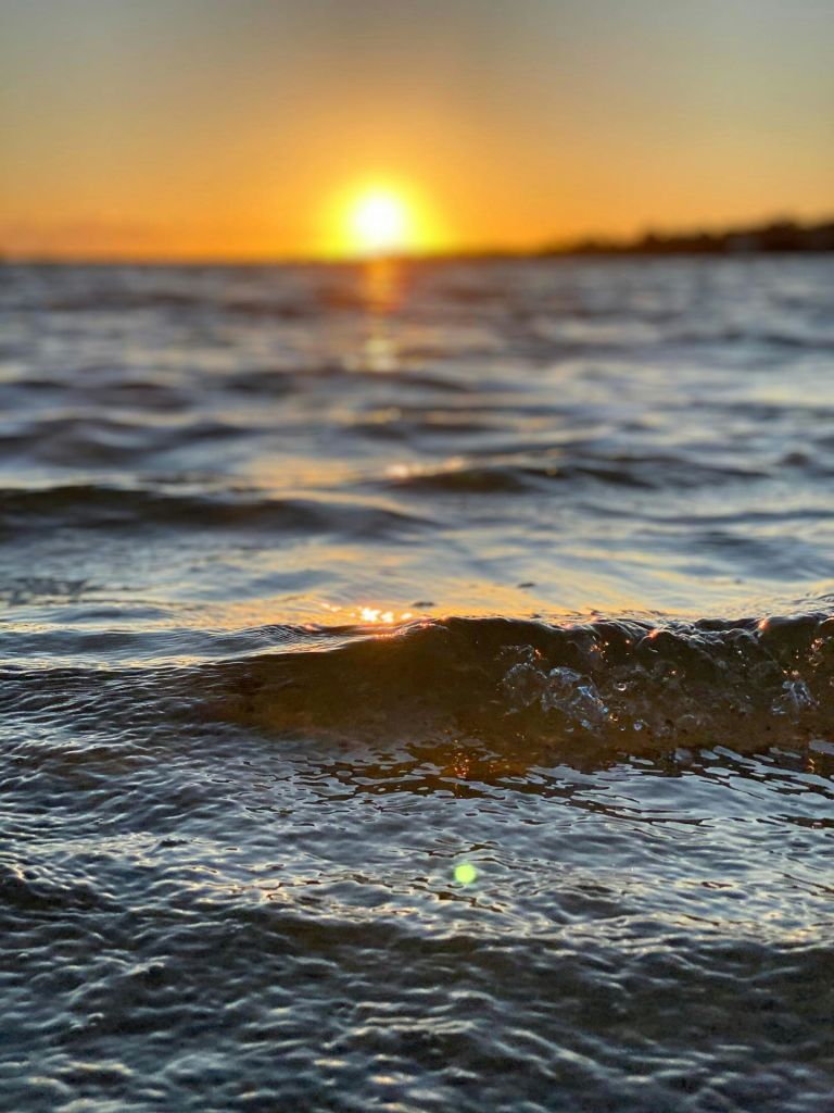 해가 지는 지평선에서 잔잔한 바다의 작은 파도가 물 건너 황금빛을 비춥니다.
