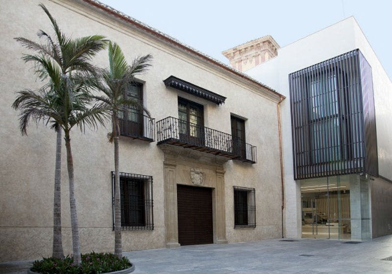 발코니, 야자수, 맑은 하늘 아래 현대적인 유리 구조가 인접한 전통적인 건물입니다.