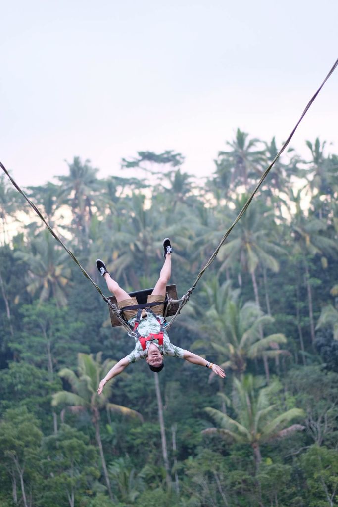 높은 야자수를 배경으로 울창한 열대림 위로 밧줄이 매달려 거꾸로 매달려 있는 사람.