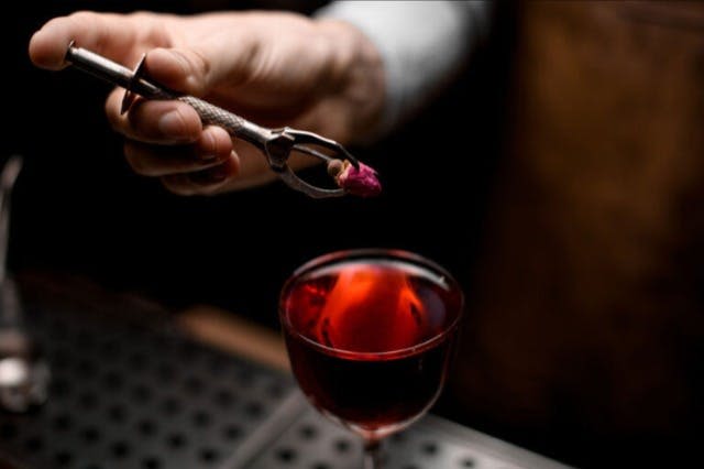 핀셋을 든 손이 작은 꽃 봉오리를 붉은 액체 잔에 넣습니다.