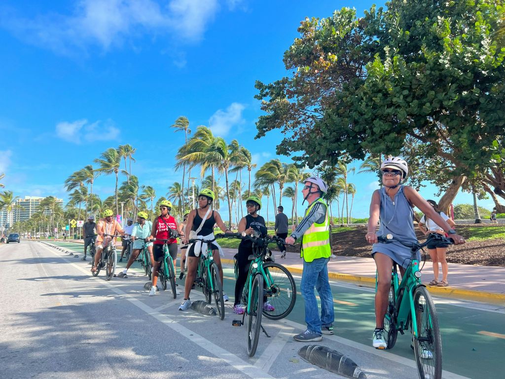 맑고 푸른 하늘 아래 야자수와 녹음이 우거진 자전거 도로에서 헬멧과 장비를 착용한 일행이 자전거를 멈춥니다.