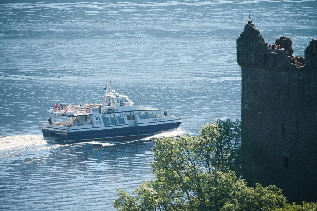 오래된 석탑 옆으로 나무가 우거진 잔잔한 바다를 가로지르는 페리.