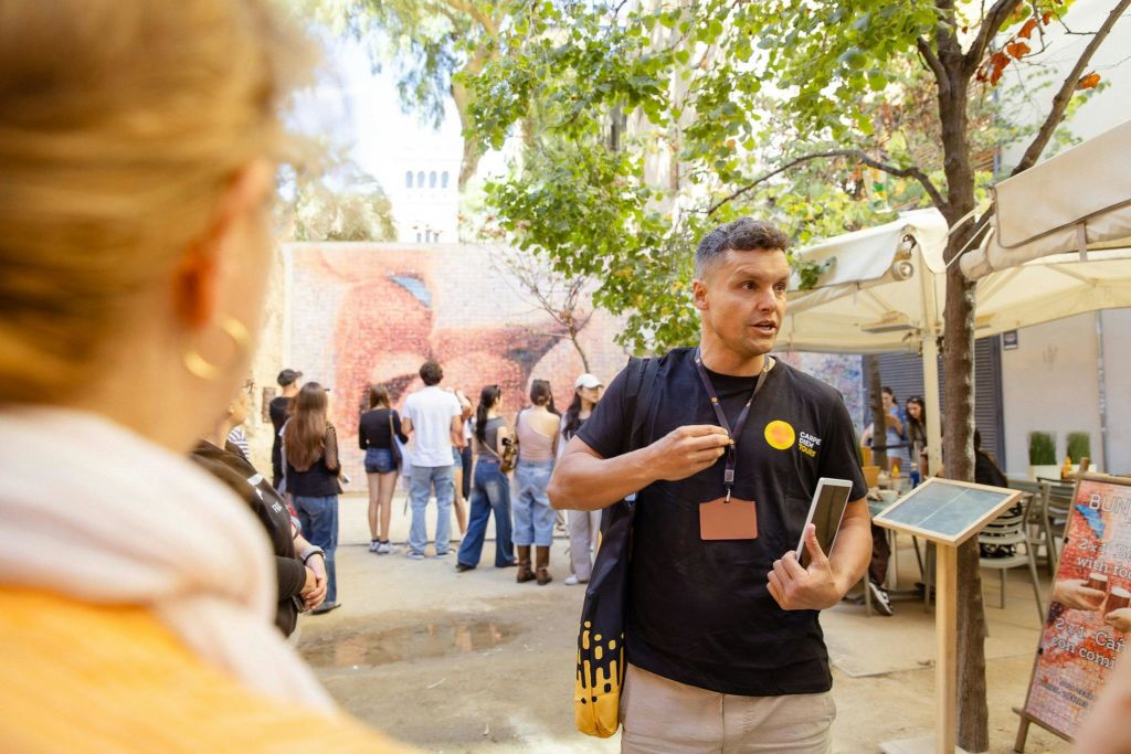 야외 공간에서 나무와 사람을 배경으로 태블릿을 들고 제스처를 취하는 남성.