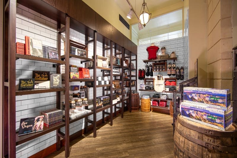 바닥에 나무 통이 있는 흰색 타일 벽에 책, 기념품, 의류가 진열된 나무 선반이 잘 정돈된 상점입니다.