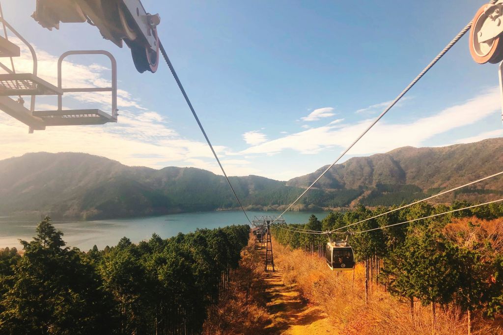 부분적으로 흐린 하늘 아래 호수와 산을 배경으로 숲이 우거진 풍경을 감상할 수 있는 케이블카 시스템입니다.