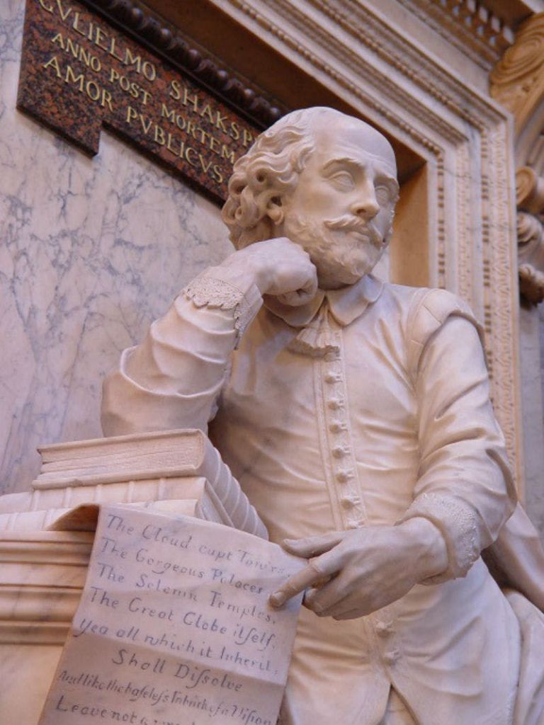 사려 깊은 표정으로 책에 기대어 수염을 기르고 곱슬머리를 한 남자의 대리석 동상. 위에 라틴 텍스트가 에칭되어 있습니다.