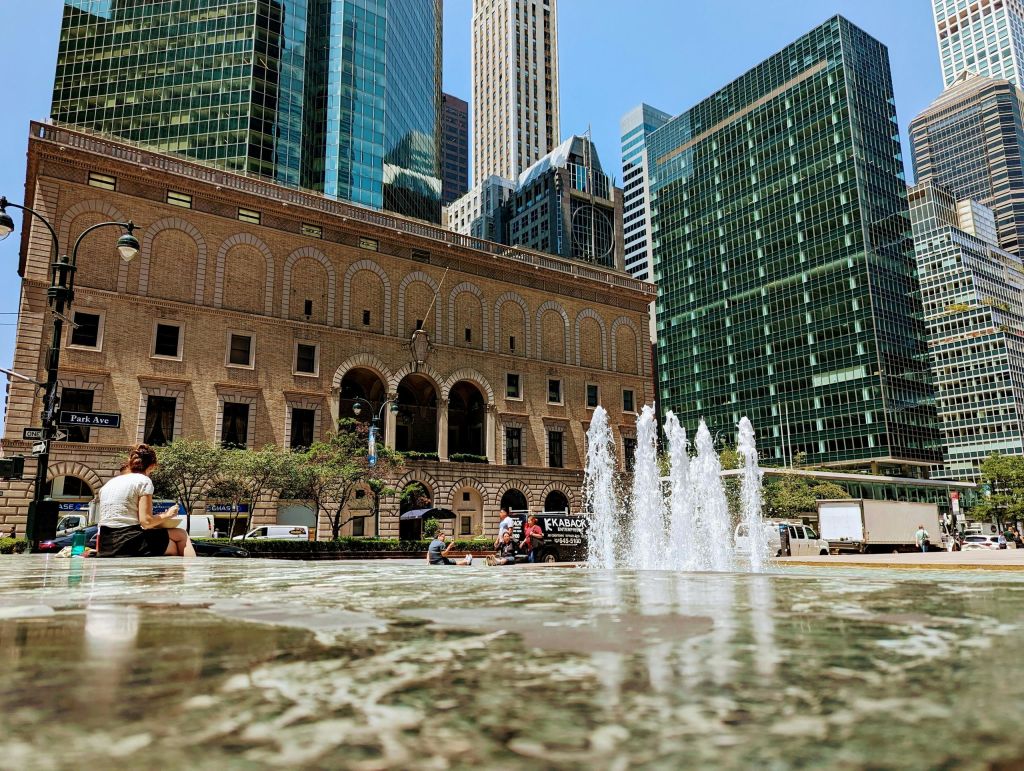 전경에 분수가 있고, 뒤에 역사적인 건물이 있으며, 배경에는 높은 현대적인 고층 건물이 있는 도시 광장입니다.