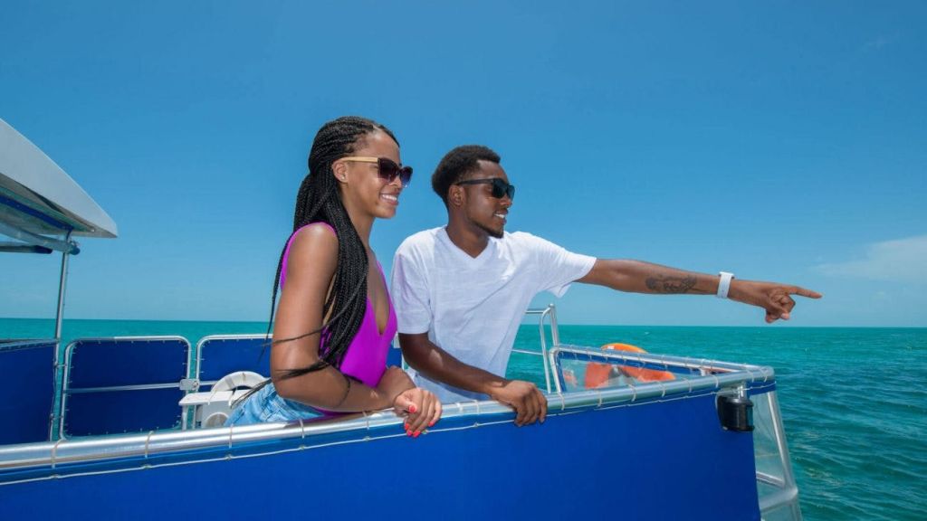 보트에서 선글라스를 쓰고, 맑고 푸른 하늘 아래 바다를 바라보며 웃고 있는 두 사람.