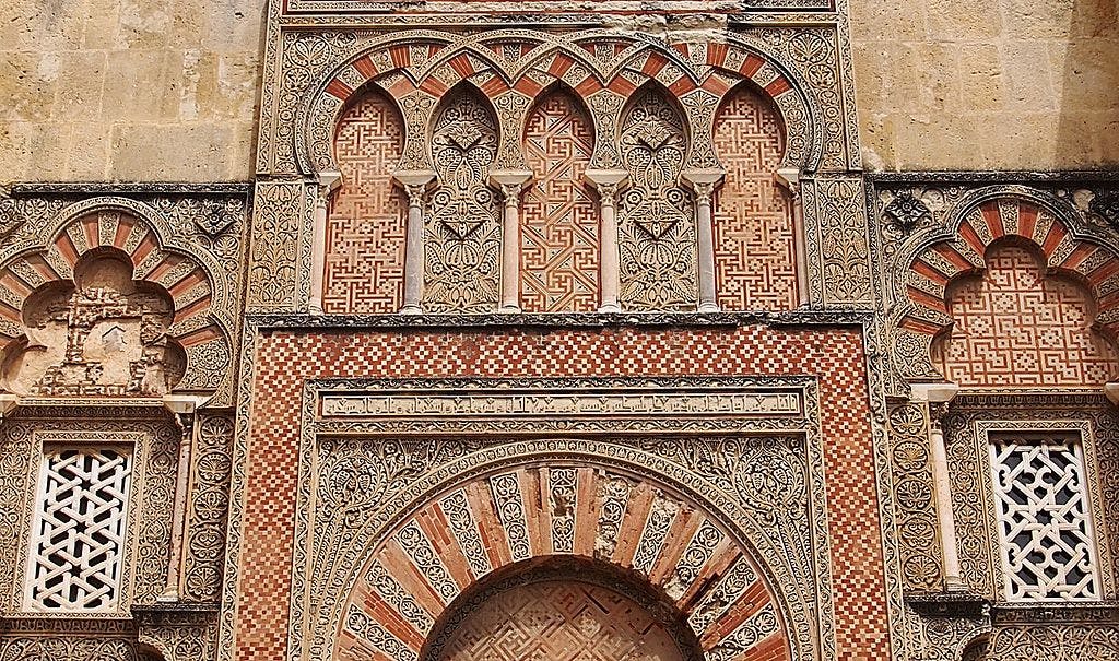 크림, 레드, 베이지 톤의 기하학적 패턴과 꽃무늬 패턴이 특징인 정교하게 장식된 아치와 외관.
