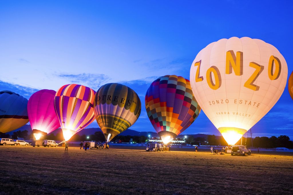 해질녘 탁 트인 들판에서 열기구가 부풀어 오르는 다채로운 색상의 열기구가 몇 사람과 차량을 둘러싸고 있습니다.